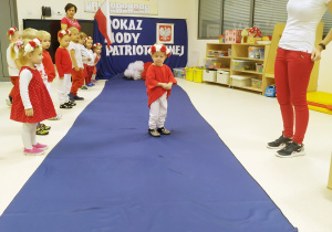 Julek ubrany na biało czerwono pozuje podczas "Pokazu mody patriotycznej" na granatowym dywanie.